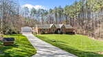 A brick house with a gray roof sits on 4126 Somerset Drive in Oxford, amid a large, neatly mowed lawn bordered by tall pine trees. A long concrete driveway leads to a detached white garage under a clear blue sky.