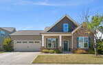 Single-story suburban house at 60 Scarlet Bell Drive in Youngsville with a two-car garage, stone and siding exterior, front porch with columns, green door, shuttered windows, and a small front yard with bushes and a tree, under a clear blue sky.