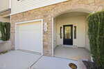 A house exterior with tan stone and siding, a white garage door, the address number 1415, an arched entryway, neatly trimmed shrubs, and a black front door with side windows.