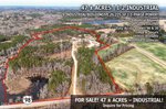 Aerial view of a 47-acre industrial property outlined in red, featuring multiple buildings, wooded areas, water features, and nearby roads. Text highlights property details, sale information, and road access to Highway 98.