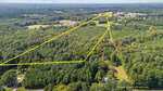 Aerial view of a large, forested area with a yellow outline indicating property boundaries. The land is densely wooded, surrounded by more trees, roads, and some scattered buildings in the distance.