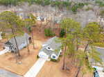 Aerial view of a suburban neighborhood with houses surrounded by tall pine trees, brown grass, and driveways; leafless trees indicate a winter or early spring season.