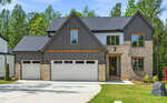 Modern two-story house with gray siding, light brick accents, and three-car garage. Large windows, gabled roof, and a covered front entry. Surrounded by trees and a neatly maintained lawn.