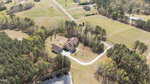 Aerial view of a large house with an attached garage, surrounded by trees and lawns, situated near a pond and bordered by rural roads and open fields.