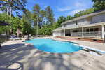 A backyard oasis at 6200 Cricket Creek Lane, Oxford, features a large swimming pool with a diving board and spacious concrete patio, surrounded by tall trees. A two-story white house with a wide covered porch overlooks the pool.