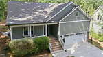 A gray single-story house with a gable roof, white trim, a covered front porch, brick steps, and an attached two-car garage. Trees and bushes surround the home.