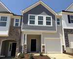 A modern two-story townhouse at 229 Alberta Drive, Franklinton, featuring gray siding, stone accents, a single-car garage, two large front windows, a black front door, and a small landscaped area with shrubs.