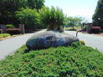 A large stone engraved with "PENINSULA" sits surrounded by greenery at the entrance of a gated community on 0 Waterstone Lane in Henderson, with trees and open gates visible in the background.