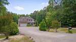 A large two-story house with a stone and siding exterior at 180 Great Woods Lane, Youngsville, features a front porch, attached garage, and sits among tall trees with a wide gravel driveway and black mailbox in the foreground.