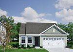 A single-story house at 215 Buckthorn Drive, Youngsville, features light green siding, white trim, a dark gray roof, and a two-car garage. The front yard has grass, small bushes, and a tree under a blue sky with scattered clouds.