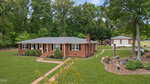 Charming single-story red-brick house at 107 Edgewood Drive, Oxford, with a gray roof, green grass and trees. Brick walkways lead to the front door and detached garage. Landscaped yard features shrubs and rocks.