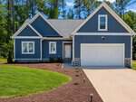 A modern blue house with white trim, stone accents, and a two-car garage at 138 Ottawa Drive in Louisburg, set against tall trees and a clear blue sky. The front yard features grass, mulch, and a paved driveway.