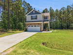 Charming two-story house at 130 Teal Drive, Youngsville, with a stone and gray exterior, attached two-car garage, front porch, and large green lawn, surrounded by tall trees under a clear blue sky.
