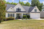 A two-story suburban house at 2796 Clifton Avenue, Creedmoor, with white siding, green shutters, a dark gray roof, double garage, and well-maintained lawn, surrounded by bushes and trees on a sunny day.