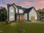 Modern two-story house at 205 Red Cardinal Court, Youngsville, with white siding, black trim, large windows, and a wood-paneled garage. A small tree with orange leaves accents the front yard beneath a pink and purple sunset sky.