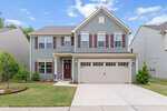 Charming two-story suburban house at 1109 Spring Meadow Way in Wake Forest, featuring blue-gray siding, white trim, maroon shutters, a double garage, manicured lawn, and inviting landscaping under a blue sky with clouds.