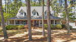 A two-story brick house in Oxford at 4509 S Highway features a large front porch, dormer windows, and a gabled roof, nestled among tall pine trees and landscaped shrubs in the front yard.