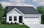 Charming single-story house at 210 Buckthorn Drive, Youngsville, featuring light siding, black shingles, two front windows, a black front door, and a white two-car garage; lush green grass and shrubs complement the trees in the background.