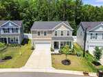 A two-story beige house at 45 Carolina Maple Drive, Franklinton, with a front porch, attached garage, and driveway sits on a green lawn with young trees, flanked by similar homes and backed by a dense forest.