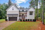 A modern two-story white house with black trim on 4535 Gresham Drive, Oxford, featuring a dark double garage, a front porch with steps, neatly trimmed bushes, and a lush green lawn surrounded by tall trees.