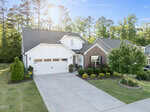 A modern suburban house at 45 Bramblewood Drive in Youngsville, featuring a two-car garage, white siding, and brick accents, is surrounded by neatly trimmed bushes, a green lawn, and trees in the background on a sunny day.