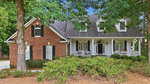 A two-story house at 237 Saddletree Road, Oxford, featuring a brick and white exterior, spacious front porch with columns, dormer windows, and a gabled roof, all surrounded by trees and landscaped shrubs.