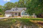 Charming single-story suburban house at 465 Spencer Gate Drive in Youngsville, featuring a gray exterior, white trim, front porch, attached garage, and a well-kept lawn bordered by tall trees under a blue sky.