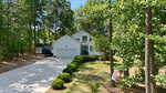 A white two-story house at 187 Buckaroo Drive in Louisburg features a blue front door, attached garage, and a long driveway. Surrounded by green trees and bushes on a sunny day, an RV is parked beside the house.