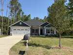 Charming single-story house in Franklinton with dark gray siding, white trim, and a double garage. Located at 20 Lemon Drop Lane, it features a grassy lawn, young tree, large rock by the driveway, and tall trees in the background.