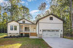 A modern white house with black trim at 124 Buckaroo Drive, Louisburg, featuring a covered front porch and large attached garage, nestled among tall trees and a green yard under a blue sky with scattered clouds.