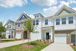 Row of modern two-story townhomes with garages on 207 Carnaby Lane in Franklinton, featuring varied facades of brick, stone, and siding, small young trees, and landscaped front yards under a partly cloudy sky.