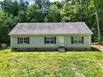 Charming single-story gray house at 126 Hunter Road, Henderson, with black shutters, a dark shingle roof, and a small front stoop with steps, surrounded by grass and tall trees under a partly cloudy sky.