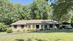Charming single-story brick house at 1080 Hedrick Drive, Henderson, with dark shutters and a gray roof. Set on a large, neatly mowed lawn with trees behind, the home features a carport and landscaped shrubs along the front.