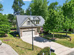 A two-story suburban house at 40 Larkspur Court, Youngsville features a stone and siding exterior, attached two-car garage, manicured lawn, and is surrounded by trees and shrubs on a sunny day. A streetlamp stands near the driveway.