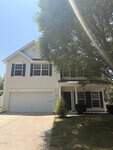 Charming two-story white house with blue shutters at 841 Stackhurst Way, Wake Forest. Features a two-car garage, covered front porch, and a large tree that partially shades the yard and driveway on a sunny day.