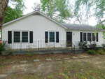 Charming single-story white house at 1536 Hight Street, Henderson, with black shutters, a black front door, and a small porch with metal railing. The front yard features stepping stones and minimal landscaping with trees and shrubs.