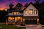 Modern two-story house at 301 W College Street in Louisburg, featuring brick and white siding, a large front porch, and two-car garage. Warm dusk lighting complements the vibrant purple and orange sunset sky, with trees surrounding the property.