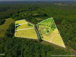 Aerial view of two green, partially wooded land parcels outlined in white, separated by a road, surrounded by dense forest and open fields under a clear sky.
