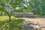 A single-story gray house at 350 Hamp Falkner Road in Henderson features a small porch, colorful flowering shrubs out front, a large shade tree, and a spacious grassy yard bordered by trees.
