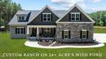 A modern custom ranch house at 185 Kenny Lane, Henderson, with stone and siding exterior, large front porch, and dormer windows, set on 26+ acres with a pond, green lawn, and wooded background.