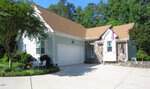 Charming single-story house at 150 Sandpipers Lane in Manson, with white siding, stone accents, a tan roof, double garage, cozy front porch with an American flag, and a driveway lined with lush greenery and trees.