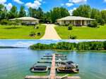 A split image: the top shows two single-story houses with garages and a driveway on a green lawn at 155 Stonewood Loop Lane in Henderson; the bottom reveals a dock with boats on a clear lake, surrounded by trees under a blue sky.