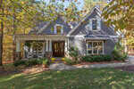 A gray house with white trim and a front porch sits amid tall trees and autumn foliage at 3587 Cotton Field Court, Wake Forest. The yard features green grass, potted flowers, and bushes lining the walkway to a wooden front door.
