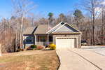 A single-story gray house at 2496 Golden Forest Drive in Franklinton features a front porch, two-car garage, and an American flag. The home is surrounded by leafless trees and a large driveway under a clear blue sky.