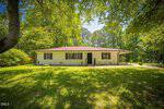 Charming single-story house at 906 Circle Drive in Creedmoor, featuring a brown roof and light-colored brick exterior. Surrounded by green grass and trees, the sunny sky casts tree shadows across the inviting front yard.