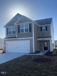 Two-story beige house with white trim, black shutters, and a double garage on 109 Long Green Way. The front yard features brown grass and a young tree. The sun shines brightly behind the roof beneath an Oxford-blue sky.