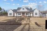 A modern, single-story house at 3414 River Manor Court in Franklinton features white siding, a dark roof, and a wide front porch with columns. The front yard has dry grass plus a few small shrubs and trees surrounding the home.