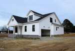 A newly constructed white two-story house with black trim, gray stone accents, and an attached two-car garage sits on a bare dirt lot at 1590 NC 96 in Franklinton under a cloudy sky.