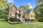 A two-story house at 3650 Pleasants Ridge Drive with red brick and cream siding, black shutters, and a gable roof, surrounded by green grass, shrubs, and trees under a blue Wake Forest sky with fluffy clouds.