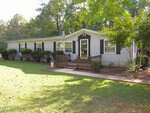 Charming single-story light gray house at 34 Waters Edge Cove, Henderson, with black shutters and a small wooden porch, surrounded by bushes and trees, and a well-maintained lawn in front.